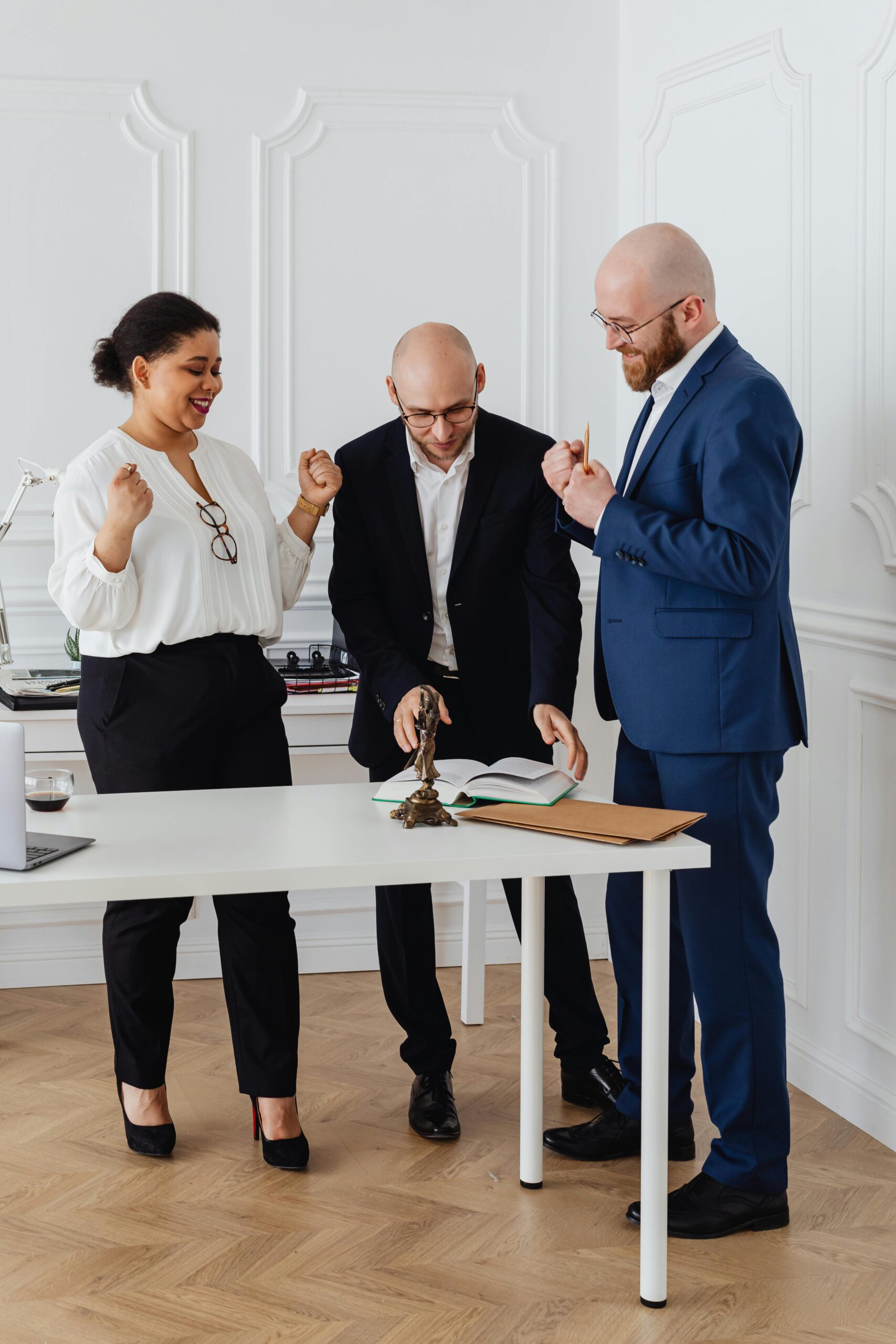 Home Three business professionals celebrate a successful deal in a modern office setting.